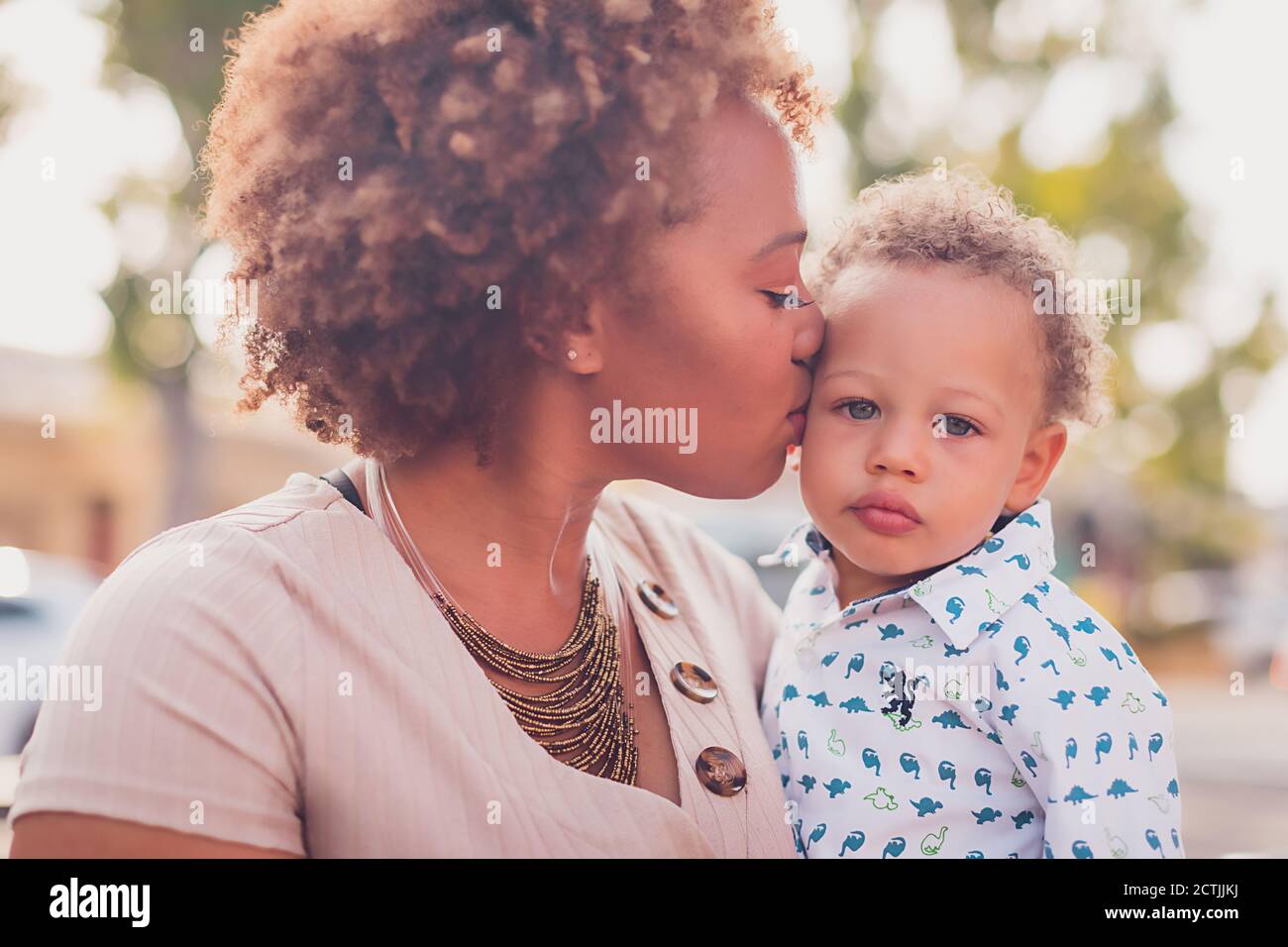 Mom holding and kissing her baby boy, baby looking at camera Stock Photo