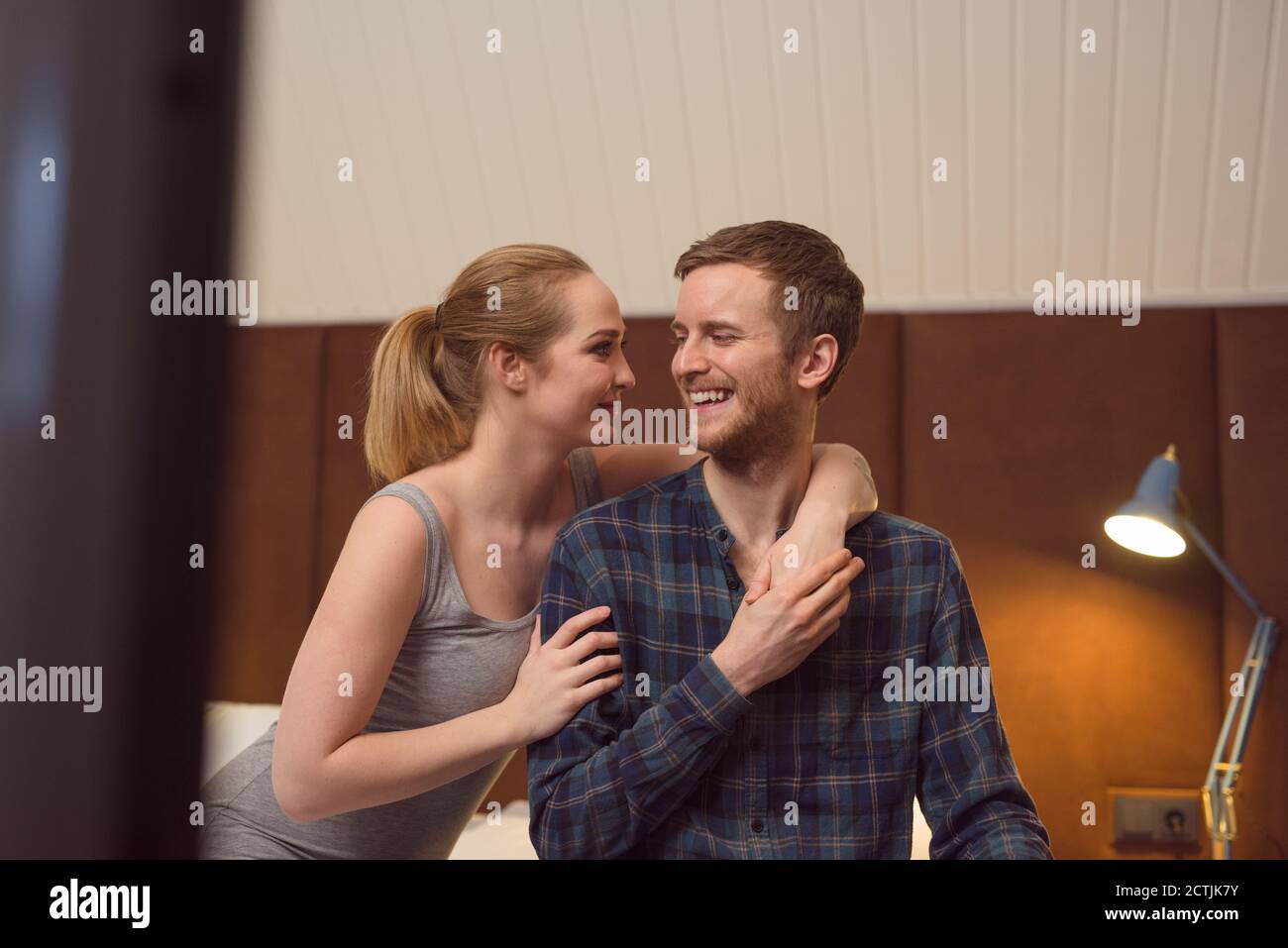 Young woman embracing happy boyfriend while sitting on bed in evening together Stock Photo