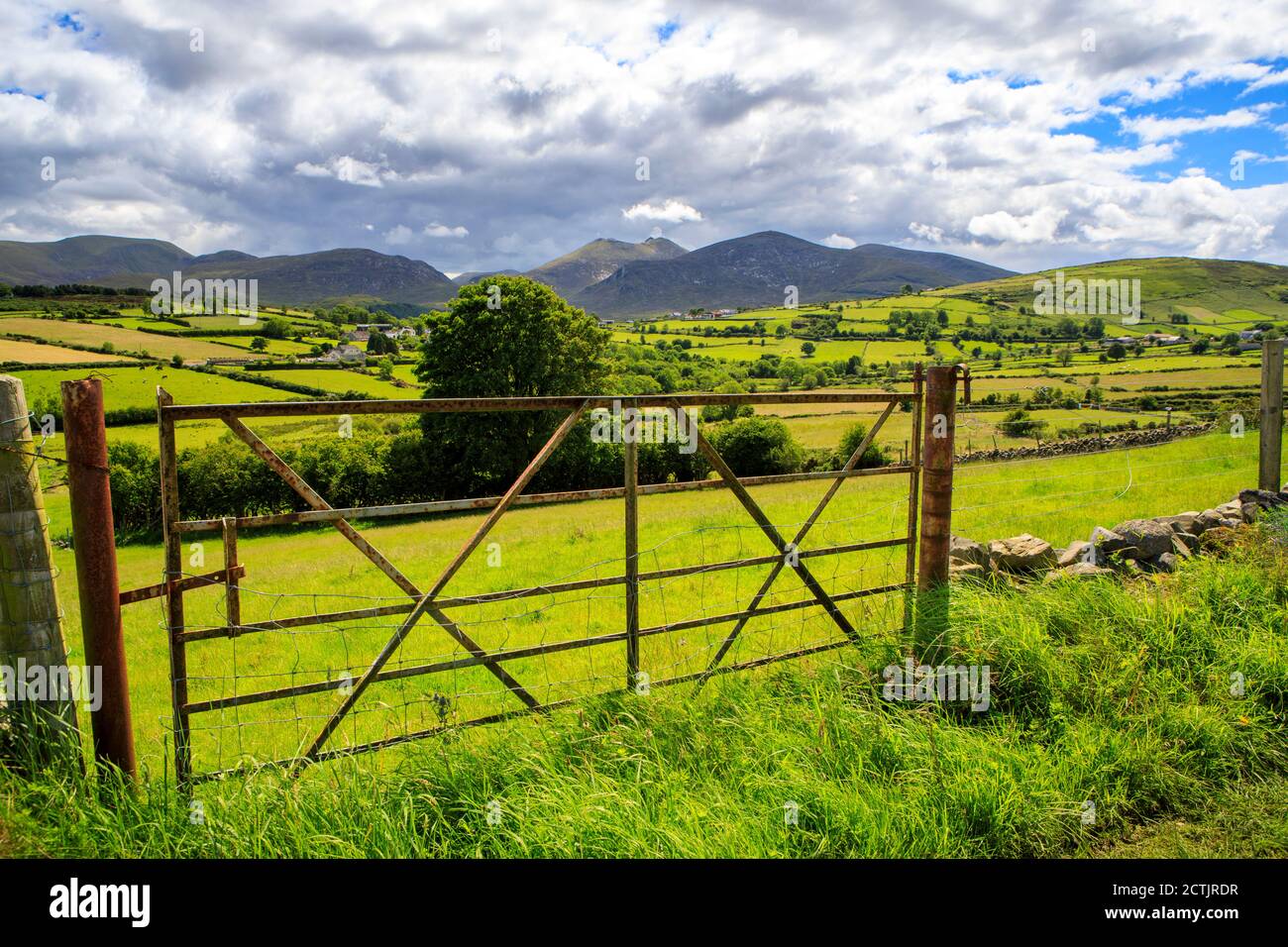 Countryside view of Northern Ireland's Mourne Mountains with green fields and gate under a cloudy blue sky. Stock Photo