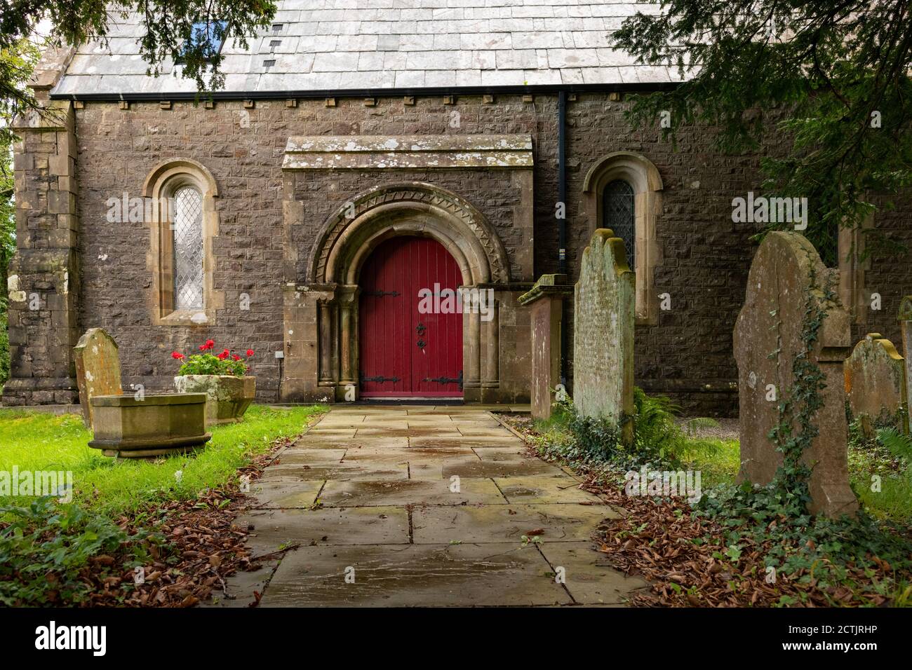 St Marys Church main doorway with pre-reformation font plant holder to left of path, Ennerdale Bridge, Lake District, Cumbria, England, UK Stock Photo