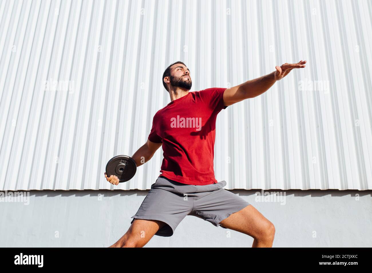 Young man practicing disc throw while standing against wall Stock Photo