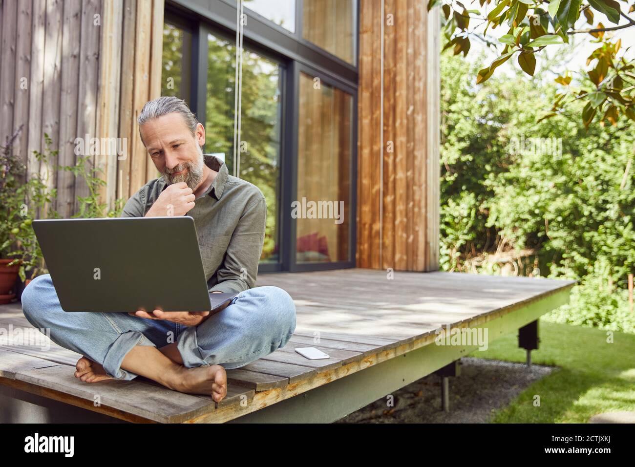 Bearded man using laptop while sitting outside house Stock Photo