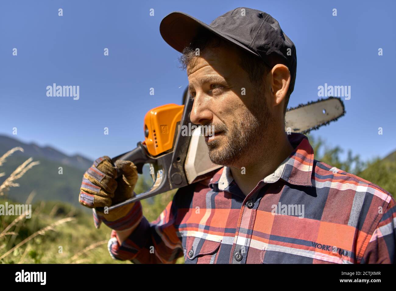 Lumberjack wearing cap while carrying electric saw on shoulder against clear sky Stock Photo