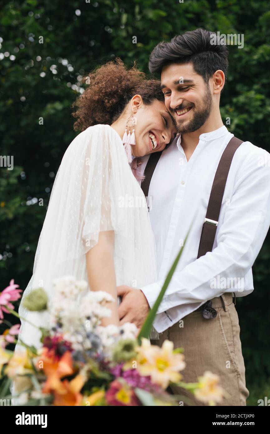 Smiling bride embracing groom while holding bouquet at garden Stock Photo