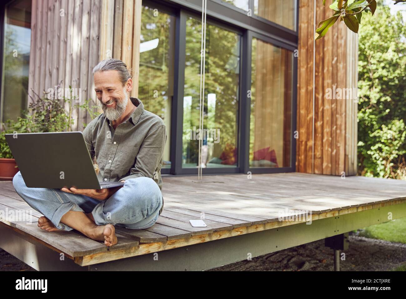 Bearded mature man using laptop while sitting outside tiny house Stock Photo