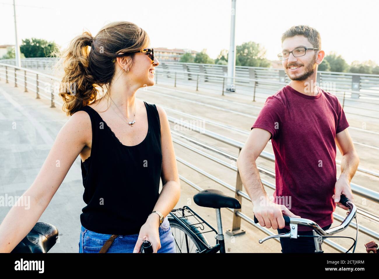 Couple talking while walking with bicycles on bridge against clear sky Stock Photo