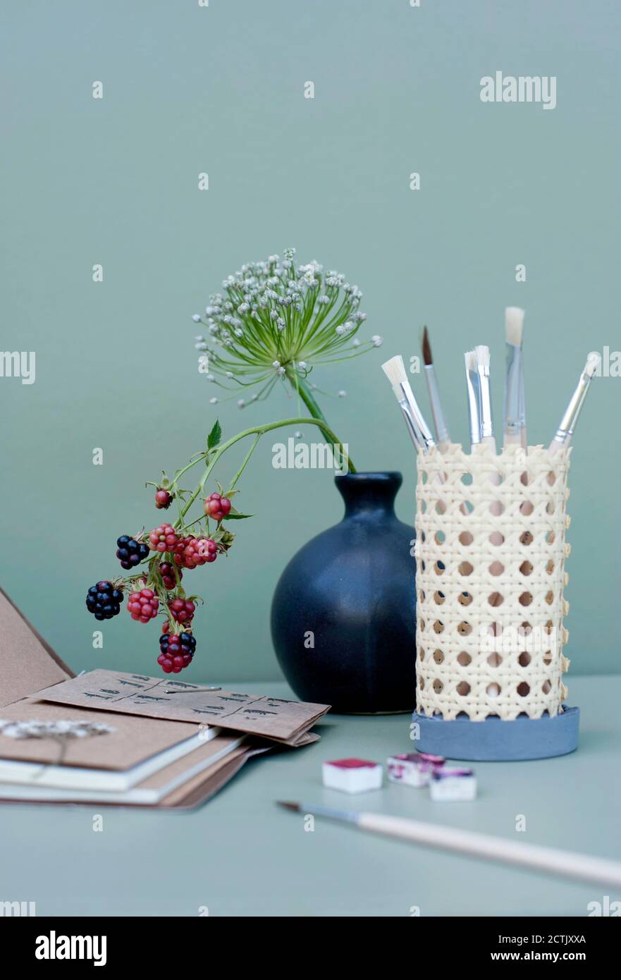 Note pad, vase with flowers and DIY rattan desk organizer with paintbrushes Stock Photo