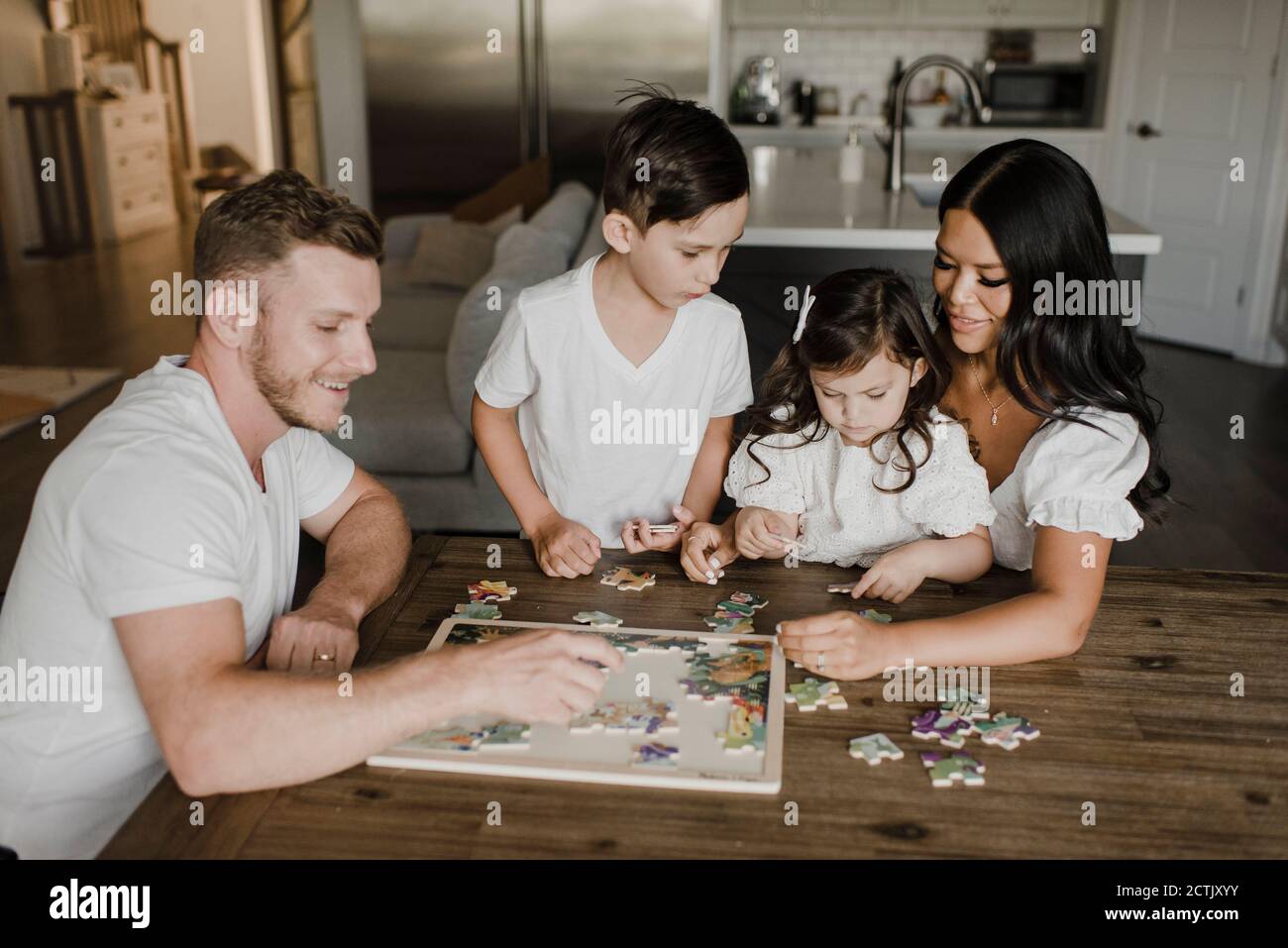 Smiling parents solving puzzle with kids over table at home Stock Photo
