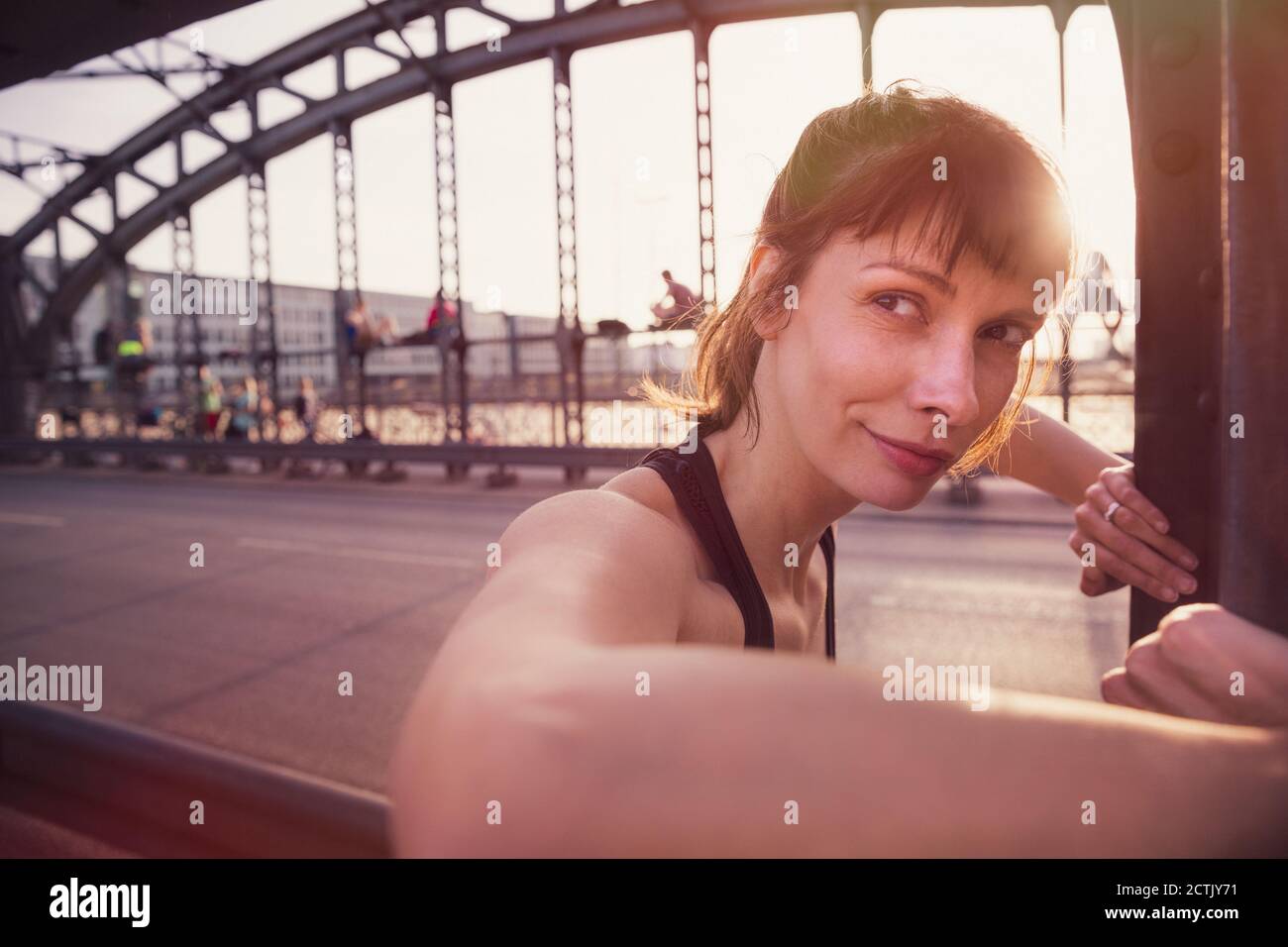 Beautiful woman looking away while exercising on bridge at sunset Stock Photo