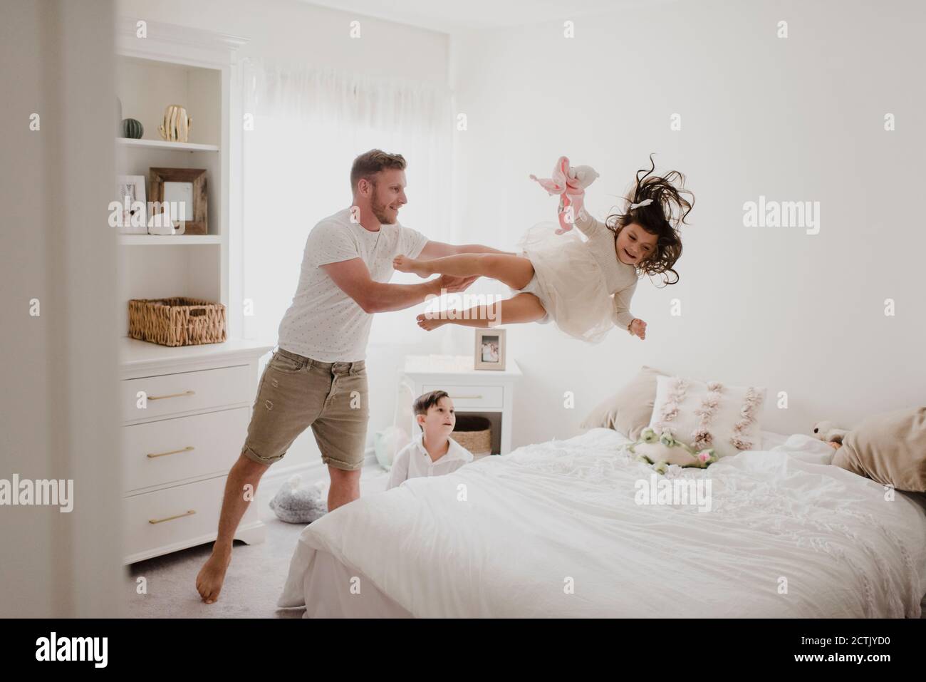 Playful father throwing daughter over bed while son sitting in bedroom