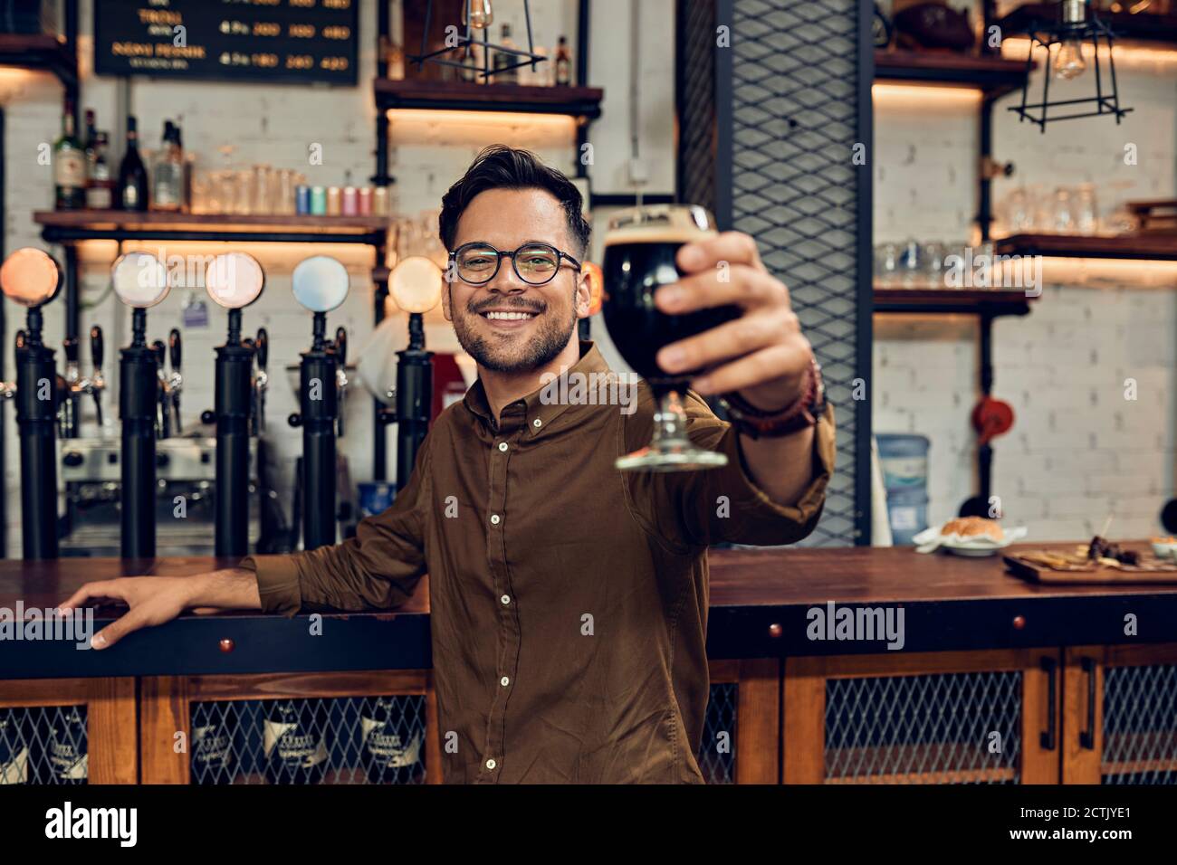 Portrait of a smiling man raising his beer glass in a pub Stock Photo