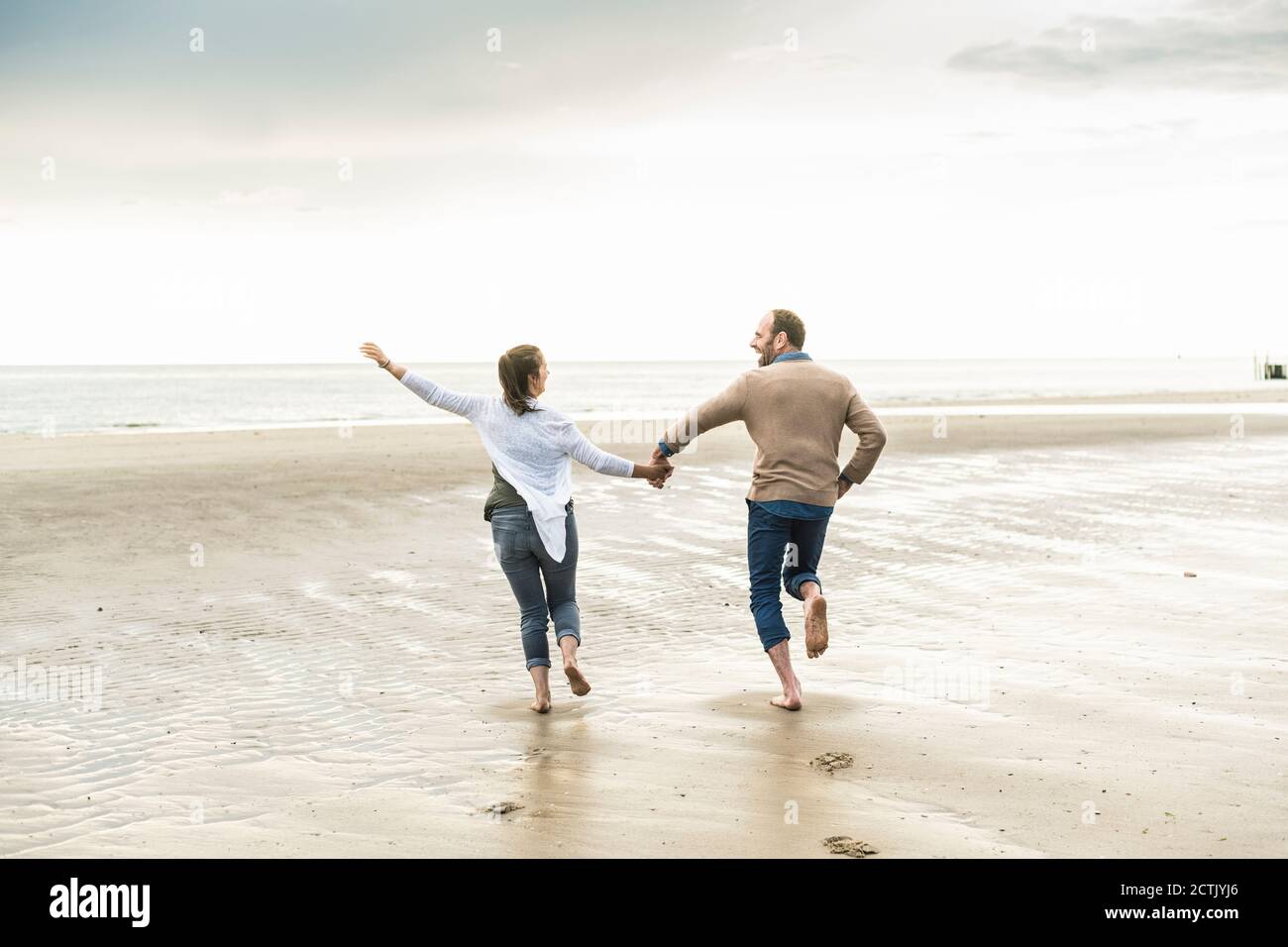 Cheerful couple holding hands while running at beach during sunset Stock Photo