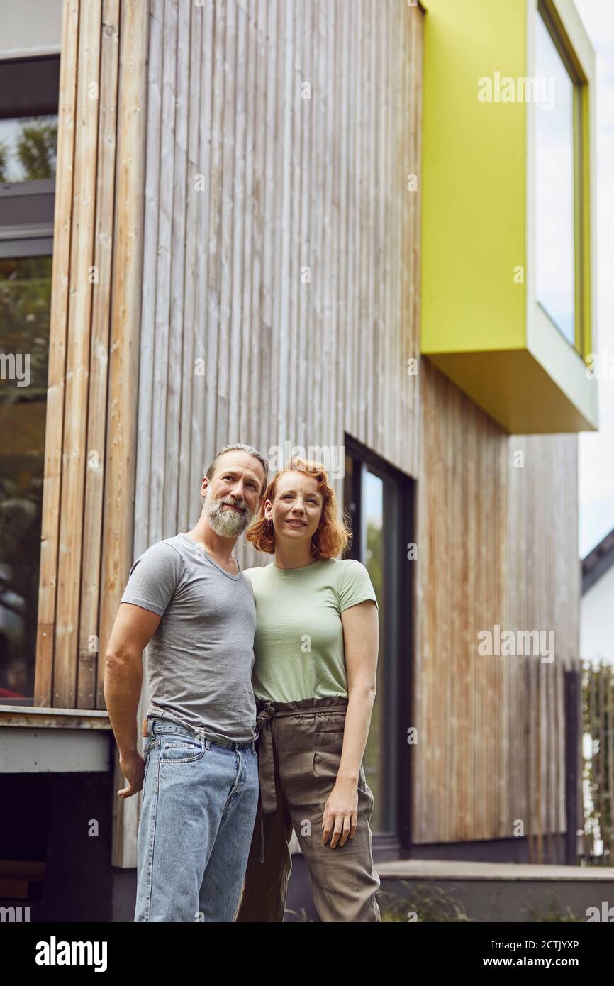 Thoughtful couple looking away while standing against tiny house in yard Stock Photo