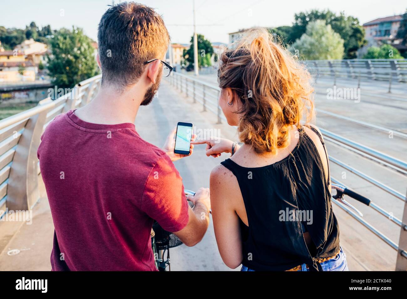 Couple using smart phone while standing with bicycles on bridge at sunset Stock Photo