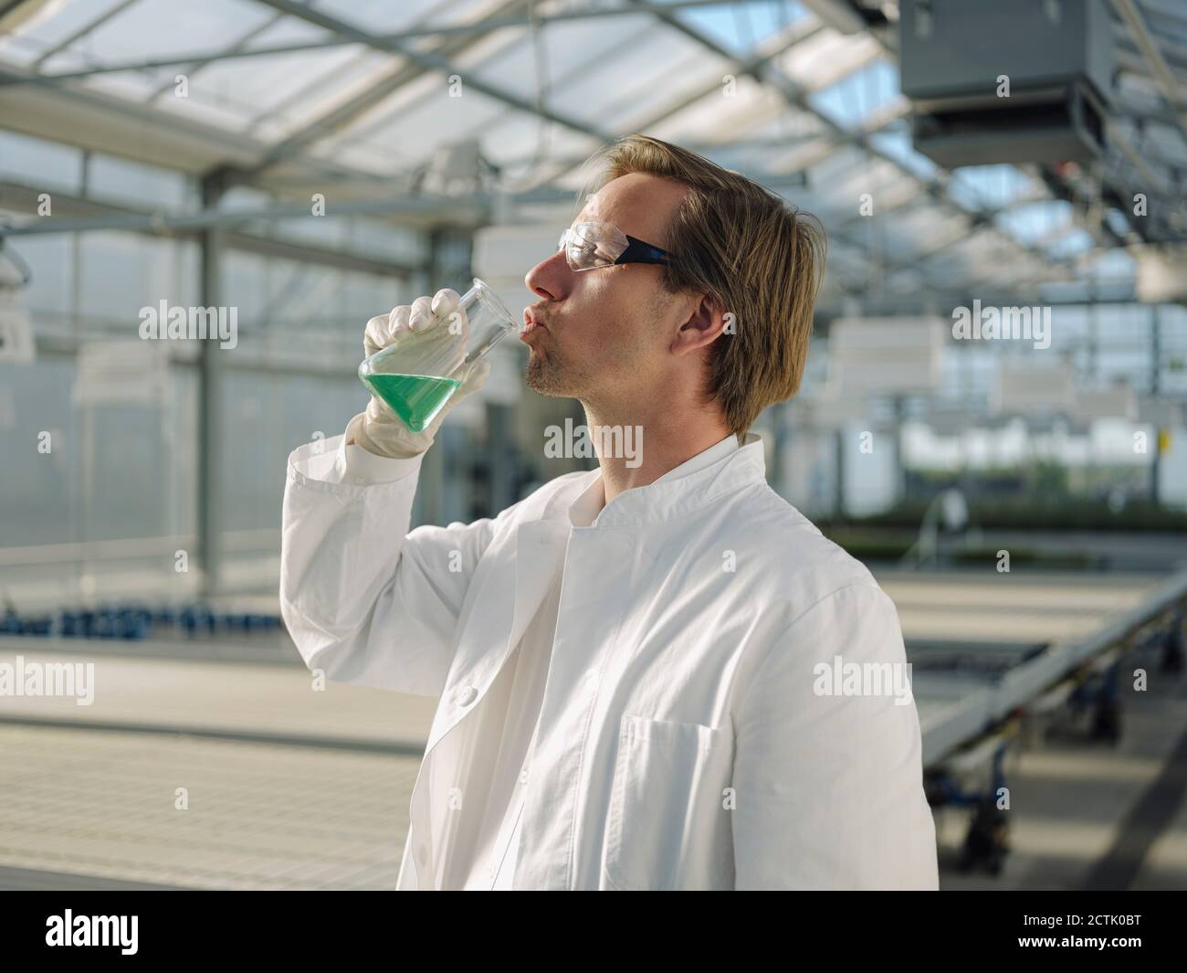 Scientist in a greenhouse drinking liquid from beaker Stock Photo Alamy