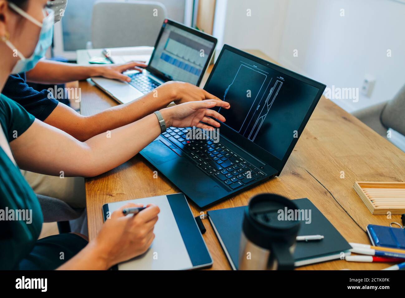Programmers discussing over laptop while wearing protective face mask at office during coronavirus Stock Photo