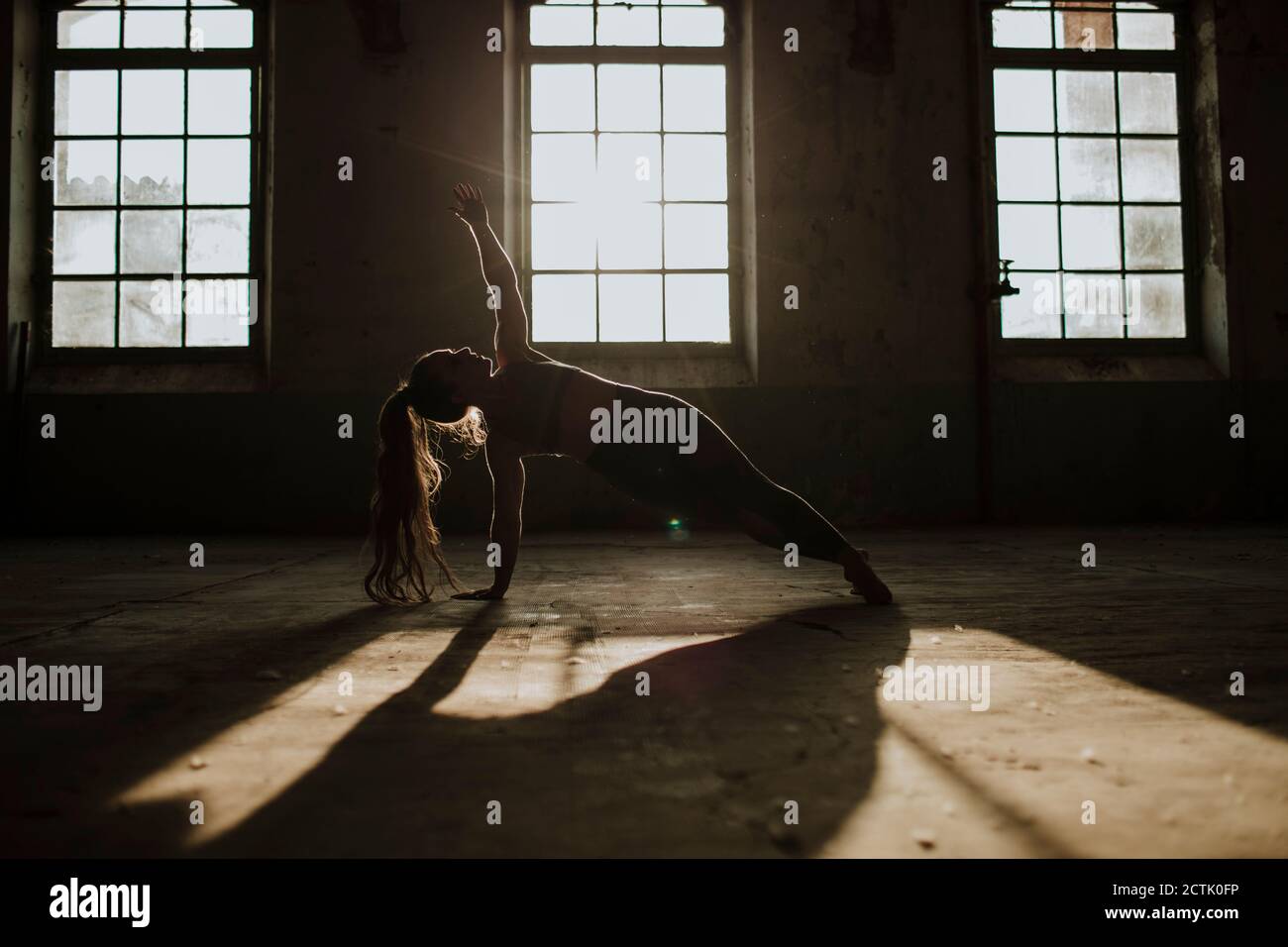 Silhouette of woman doing side plank on floor at abandoned factory Stock Photo