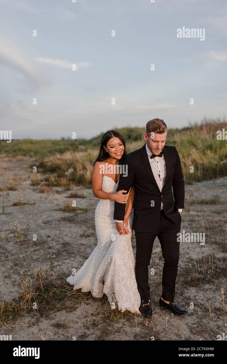 Smiling bridegroom holding hands while walking in field Stock Photo