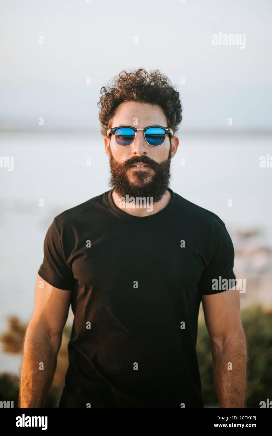 Bearded man wearing sunglasses while standing against lake Stock Photo