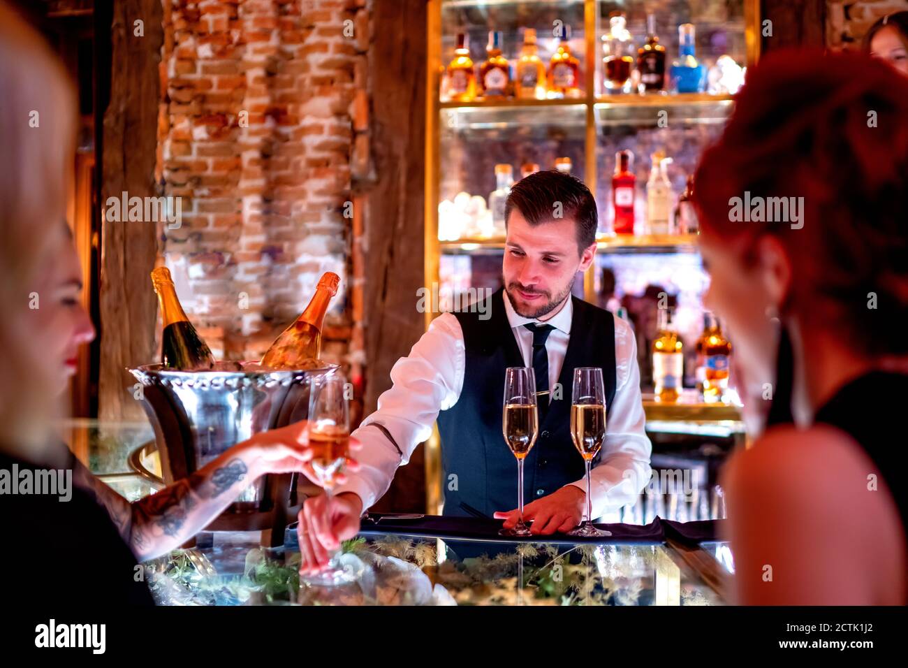 Bartender serving drink to women at bar counter in pub Stock Photo