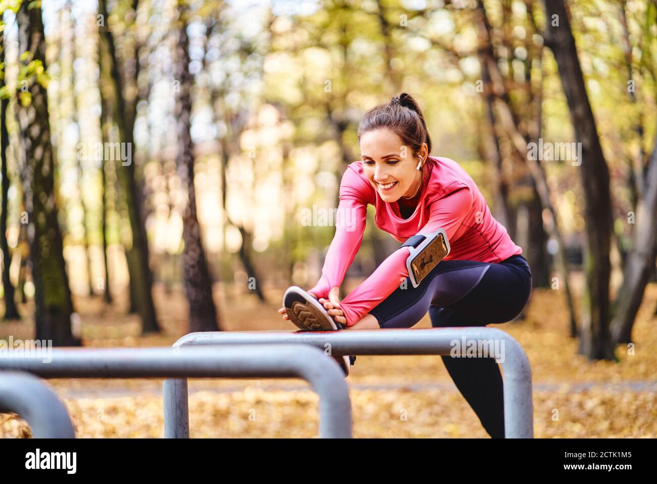 Young female jogger stretching her leg on bicycle stand in autumn forest Stock Photo