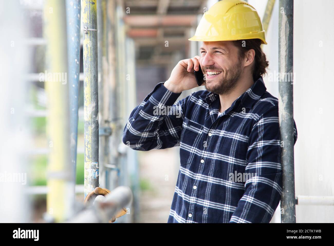 Construction worker talking over smart phone while standing by scaffold at construction site Stock Photo