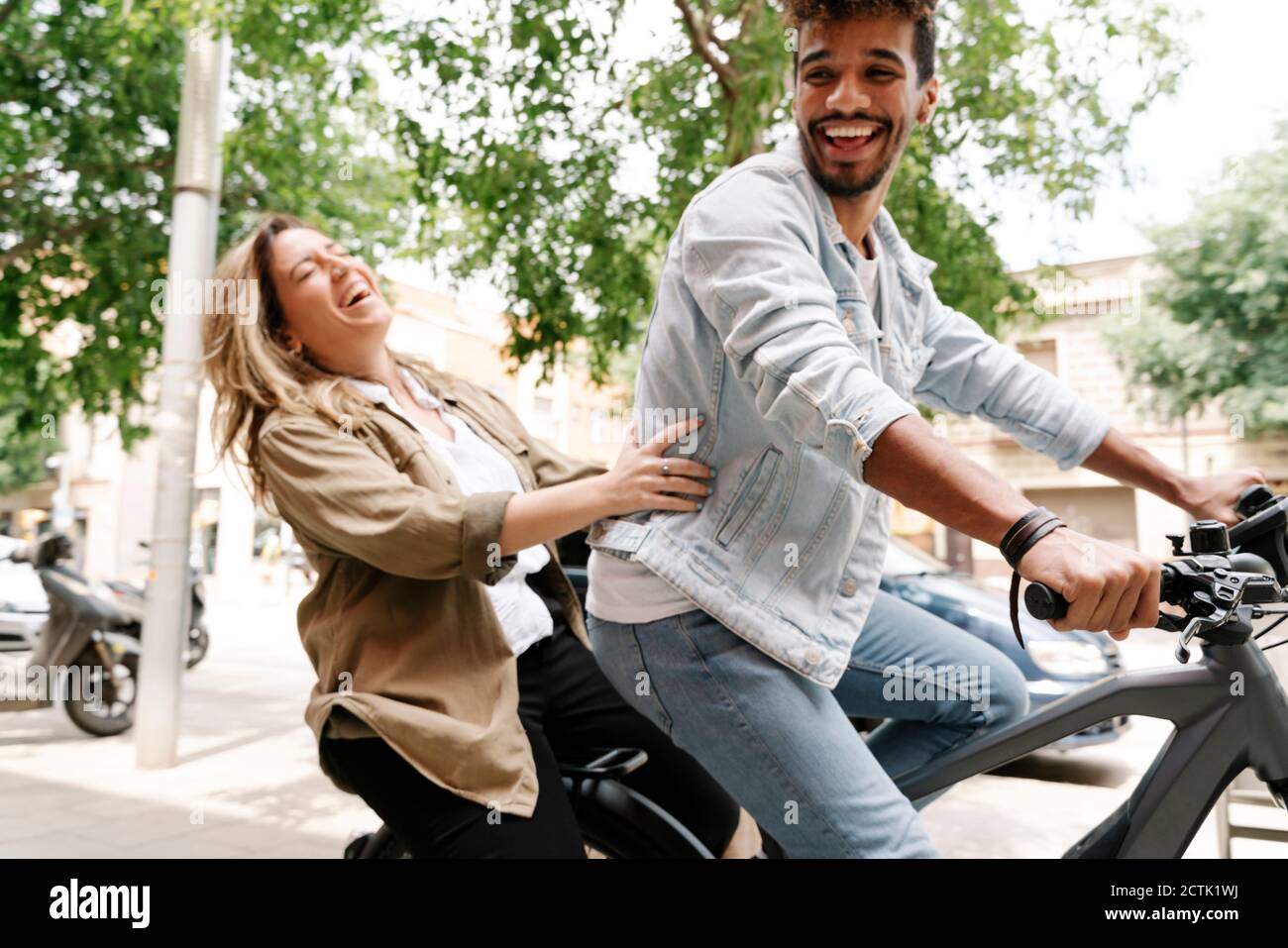 Cheerful young couple enjoying ride on electric bicycle in city Stock Photo
