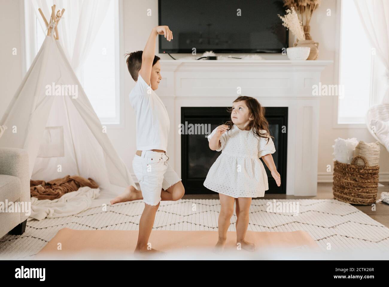 Sister looking at brother standing on one leg in living room Stock Photo