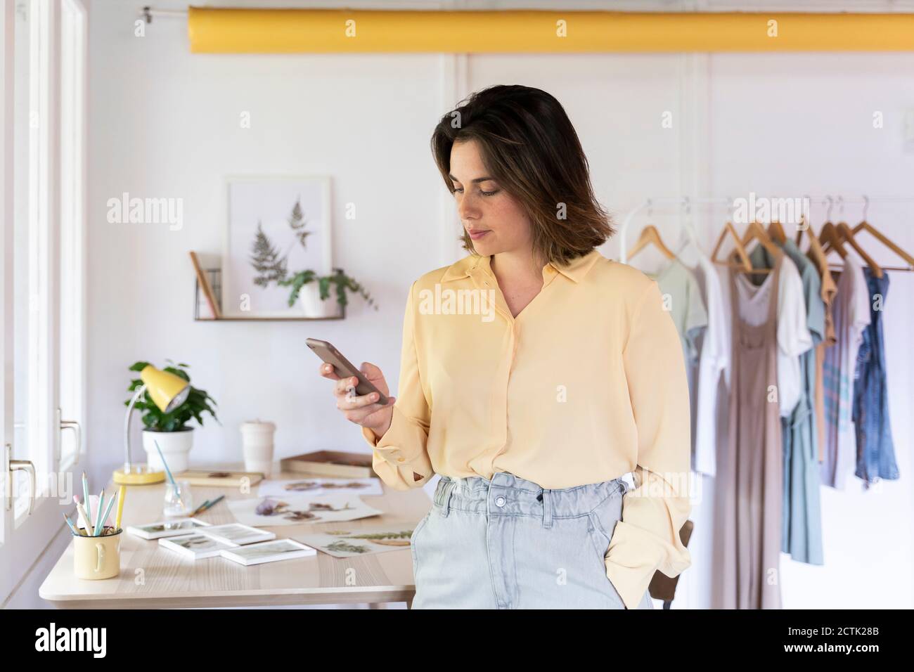 Beautiful young businesswoman using smart phone while standing at clothing store Stock Photo