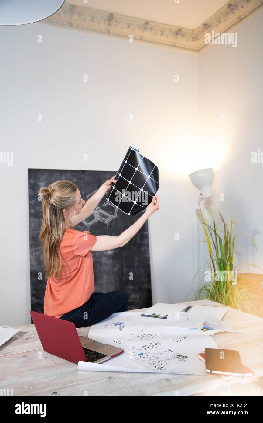 Woman sitting on desk in office looking at printout Stock Photo