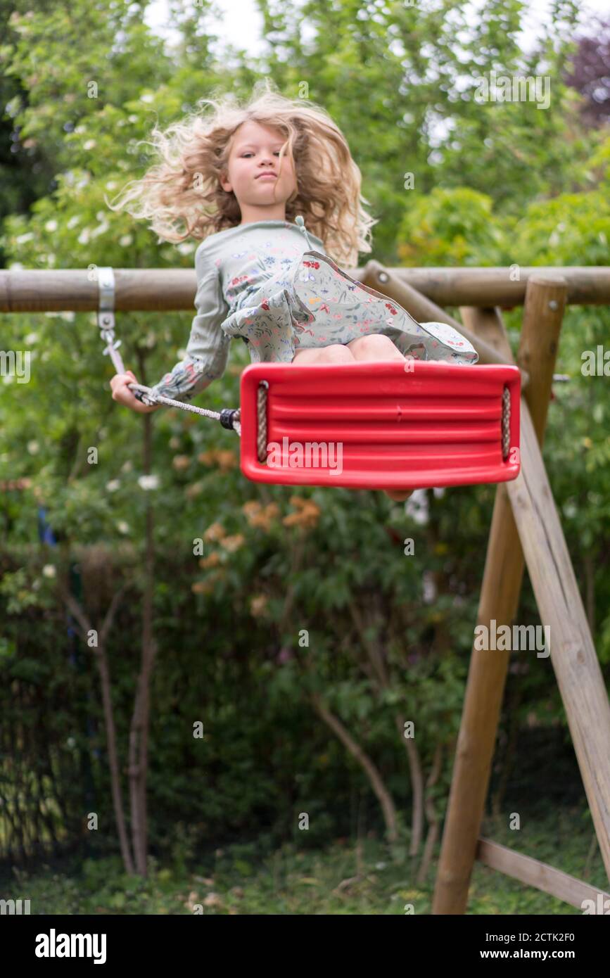 Blond girl enjoying swing at back yard Stock Photo