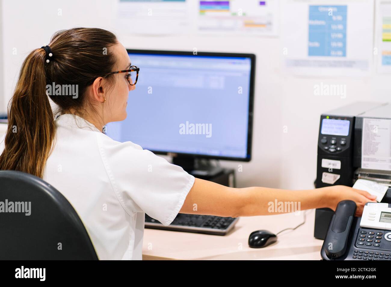 Female pharmacist using fax machine on desk while sitting in hospital Stock Photo