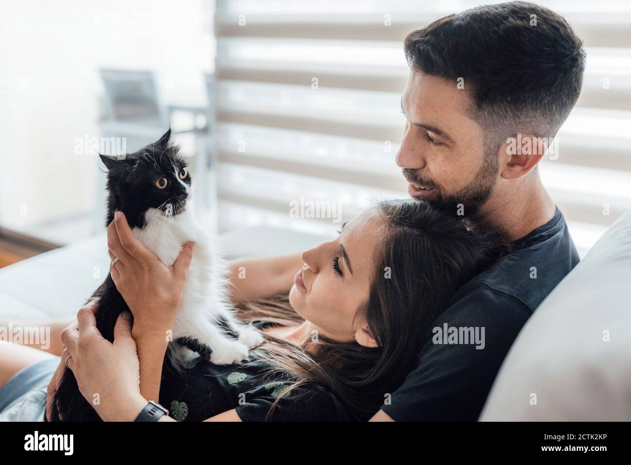 Couple sharing tenderness with cat while sitting at home Stock Photo