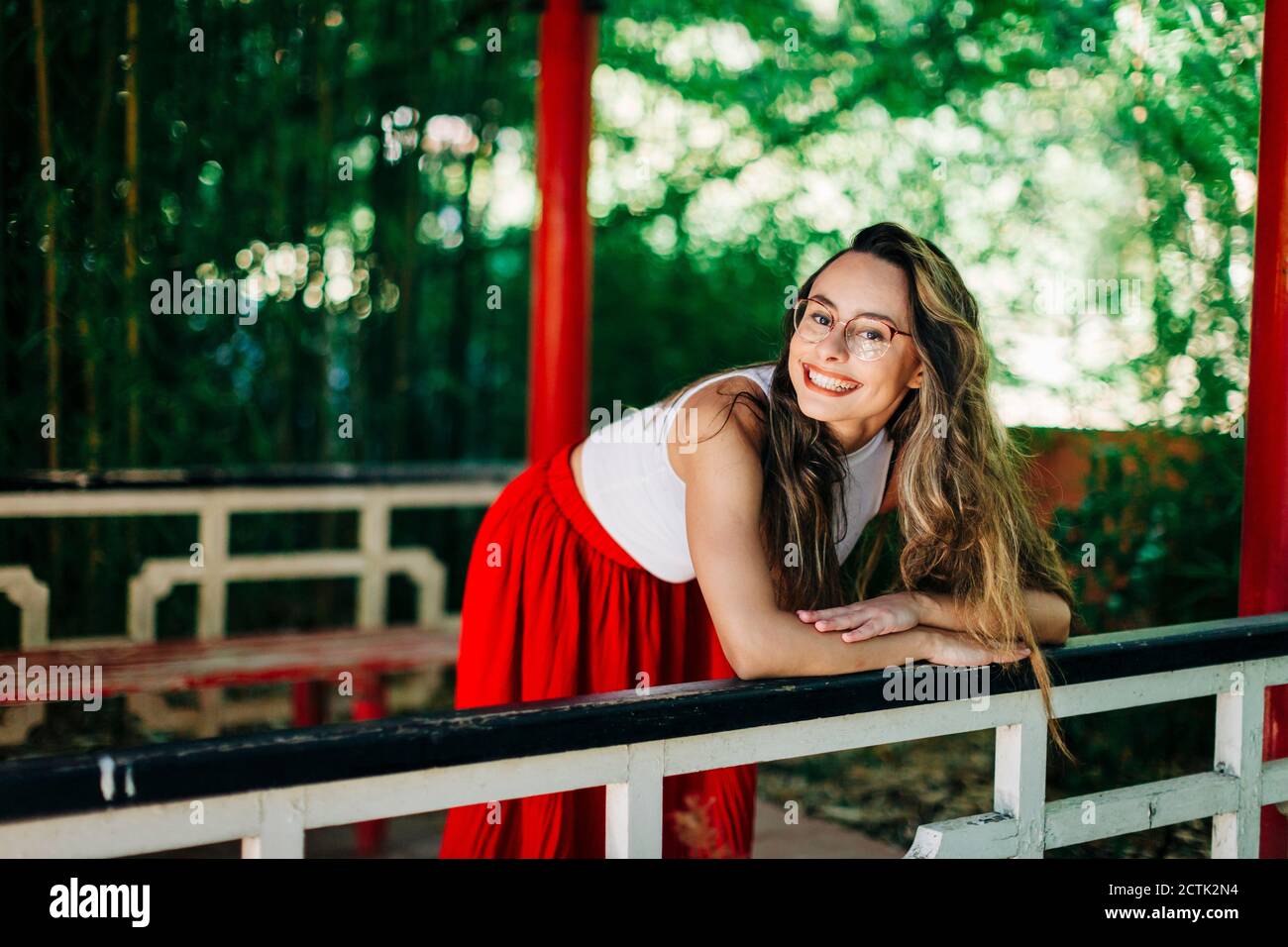 Smiling young woman with long hair standing by railing on footbridge in ...