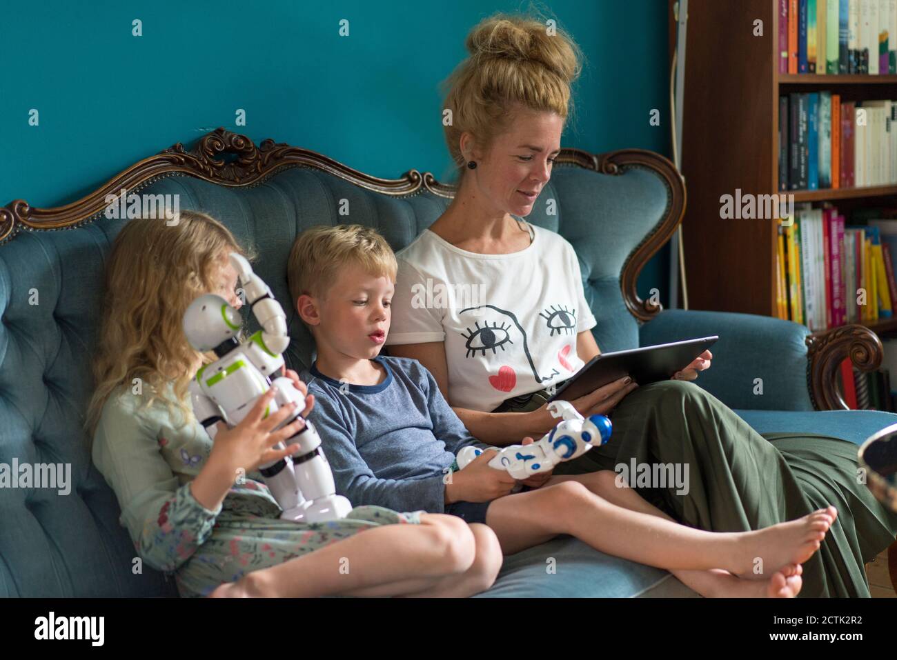 Woman using digital tablet while kids with robots sitting on sofa in living room at home Stock Photo