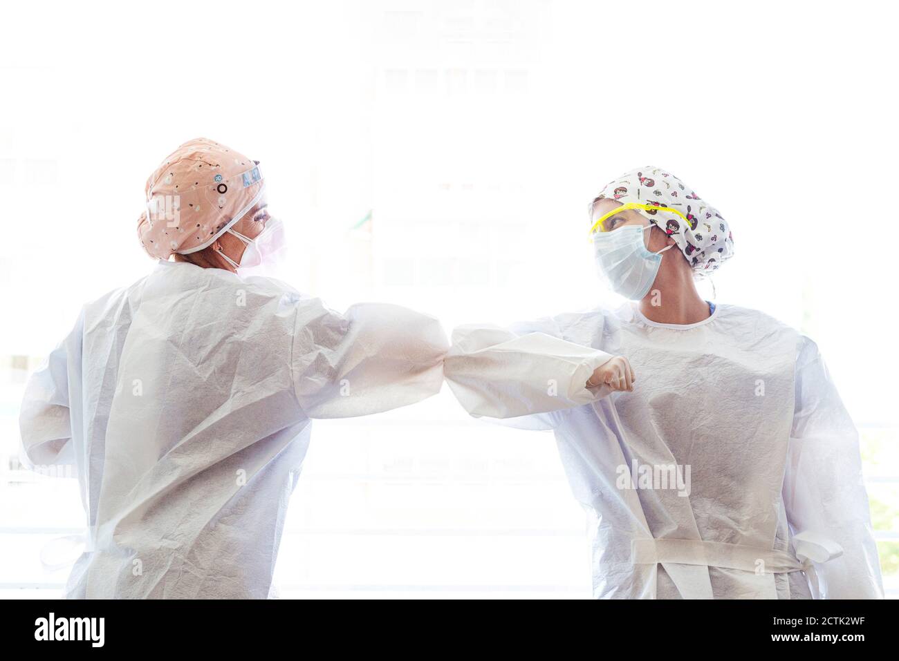 Doctor and assistant greeting with touching elbow while standing against window Stock Photo