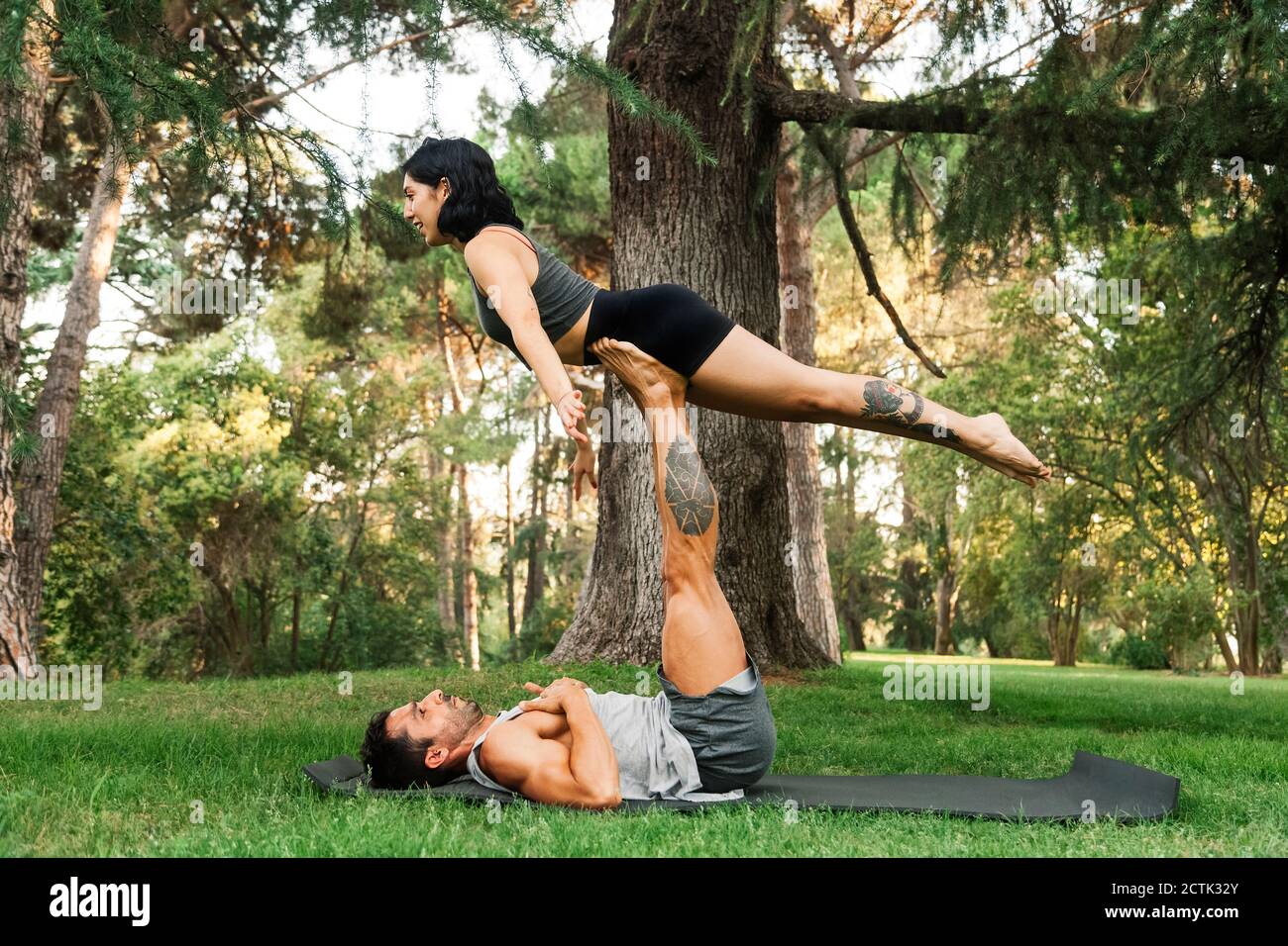 Man balancing girlfriend on legs while practicing acroyoga in park Stock Photo