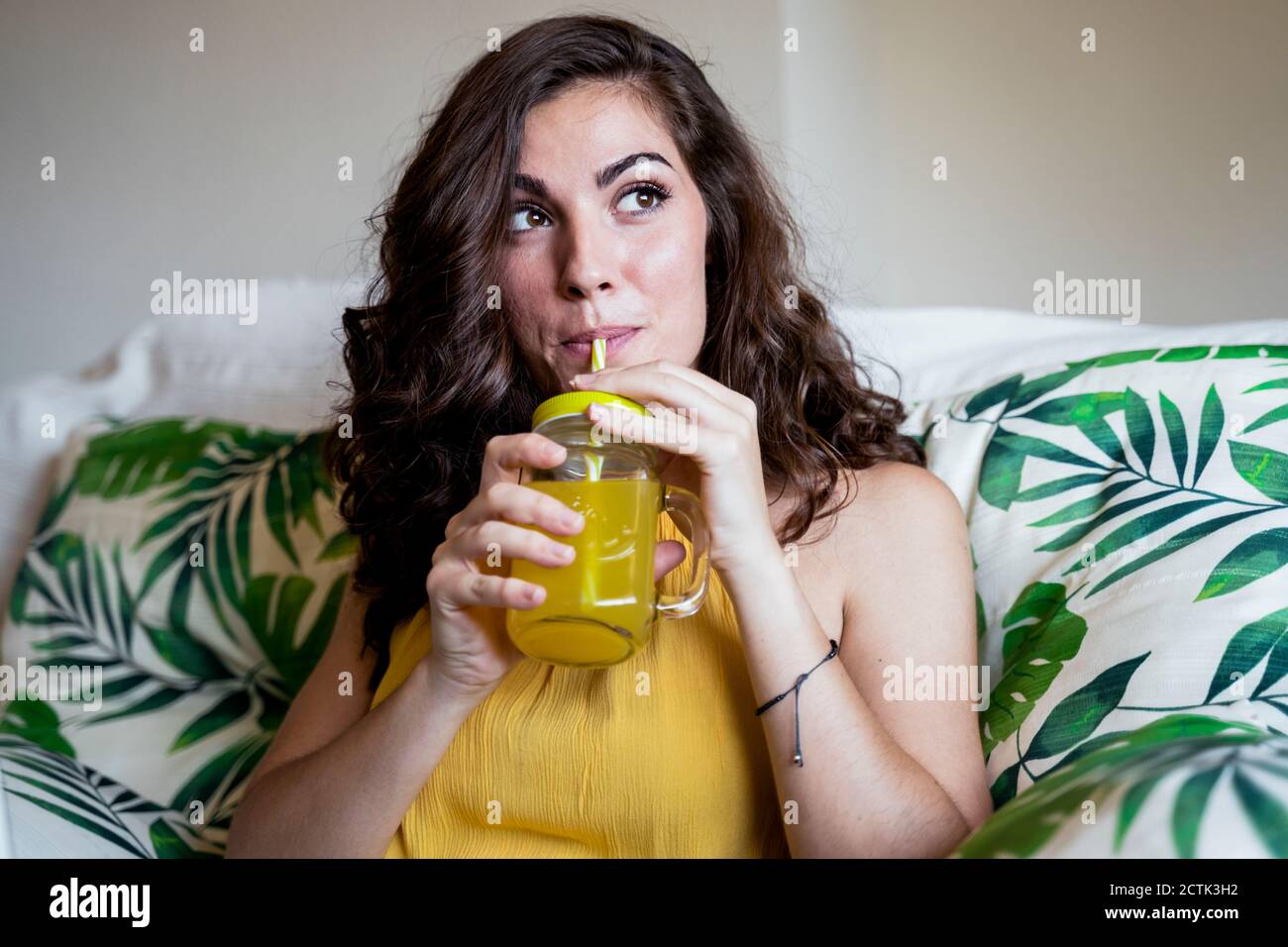 Beautiful young woman with long brown hair sipping juice from straw in mason jar while looking away Stock Photo