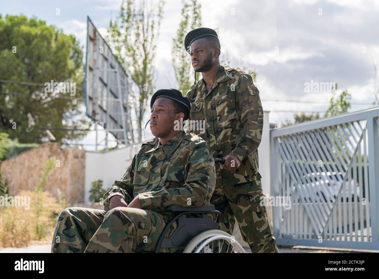 Serious army soldier helping another military officer sitting on wheelchair Stock Photo