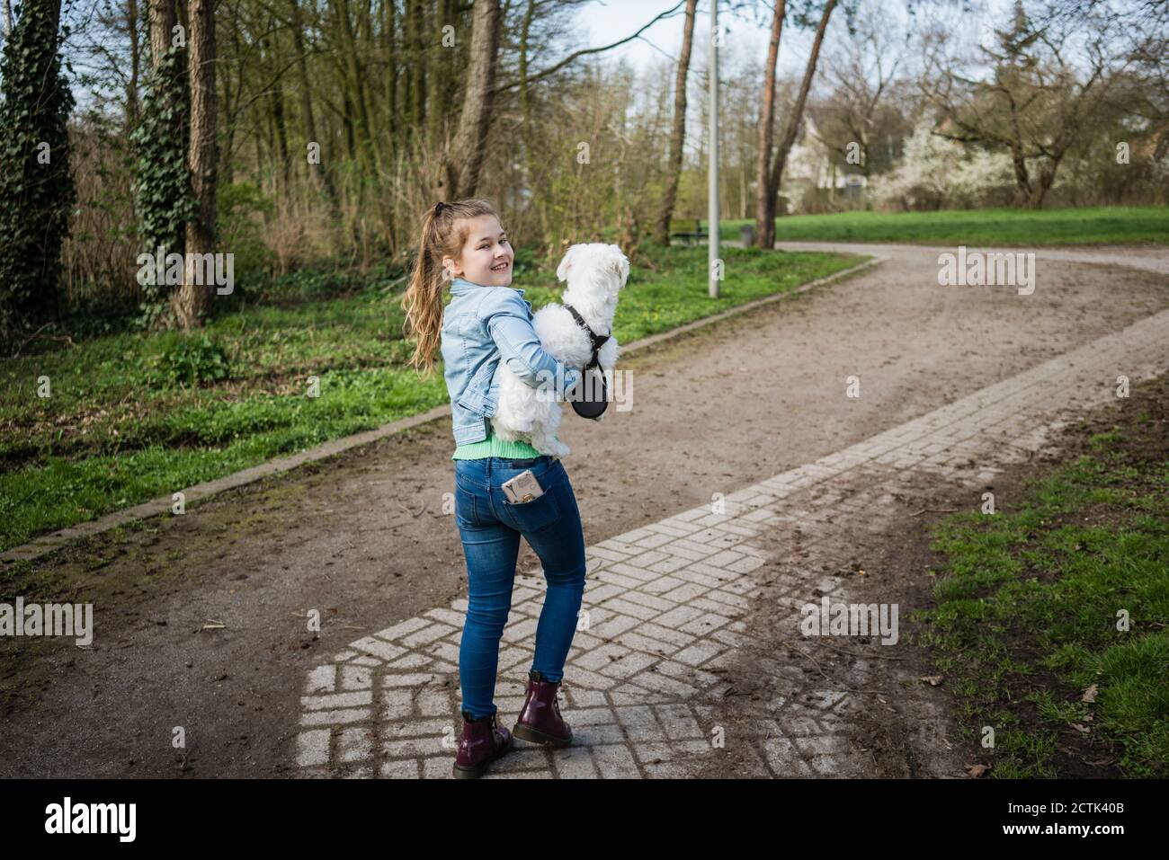 Smiling cute girl with dog walking on footpath Stock Photo
