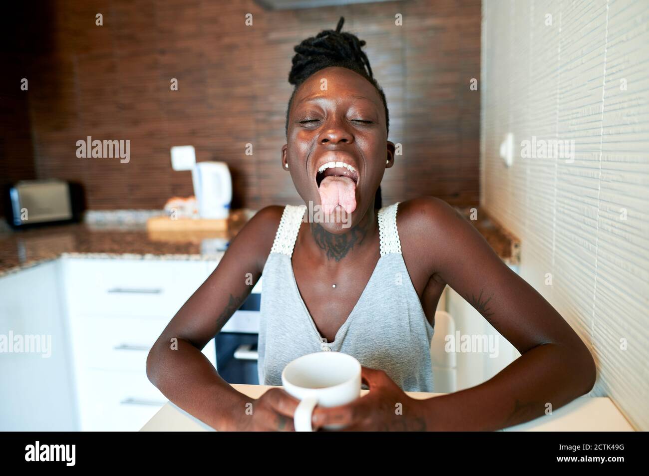 Hipster woman with forked tongue having coffee in kitchen Stock Photo