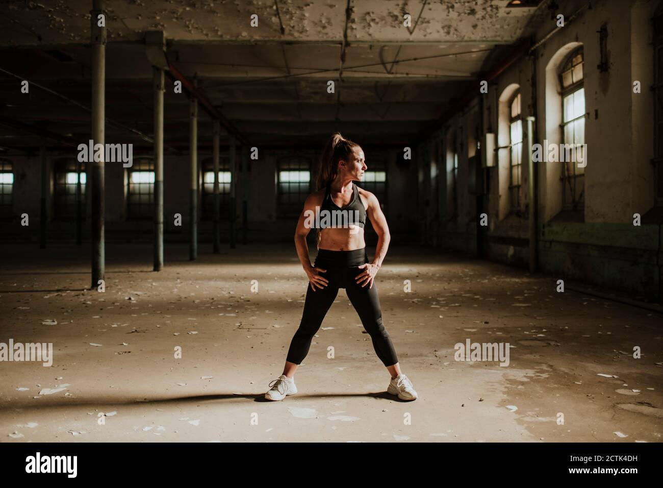Muscular build woman standing with hand on hip at abandoned factory Stock Photo