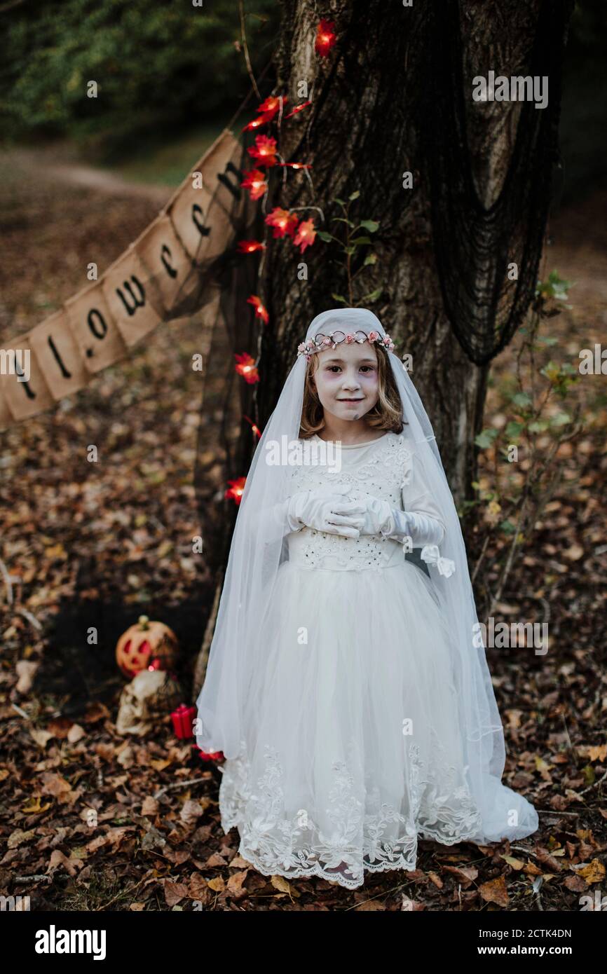 Little girl standing while wearing corpse bride costume against tree in forest Stock Photo