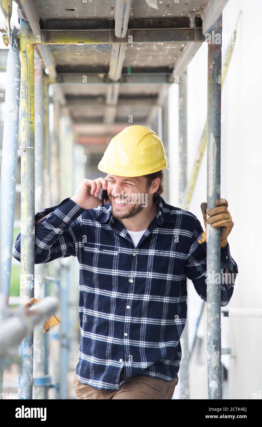 Construction worker talking over smart phone while standing by scaffold Stock Photo