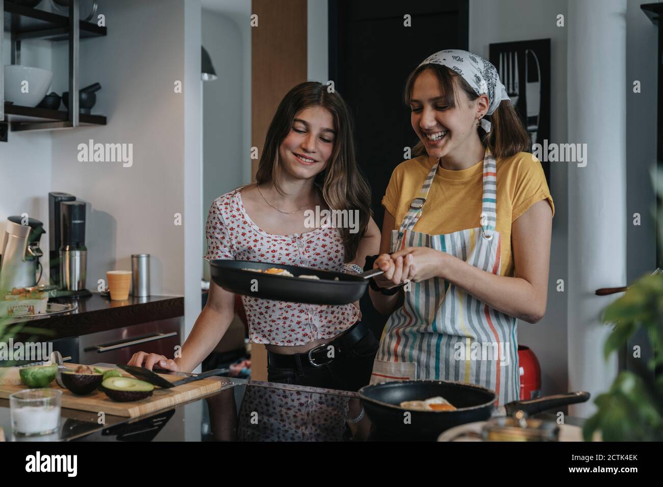 Girlfriends preparing healthy lunch together, frying eggs in kitchen Stock Photo