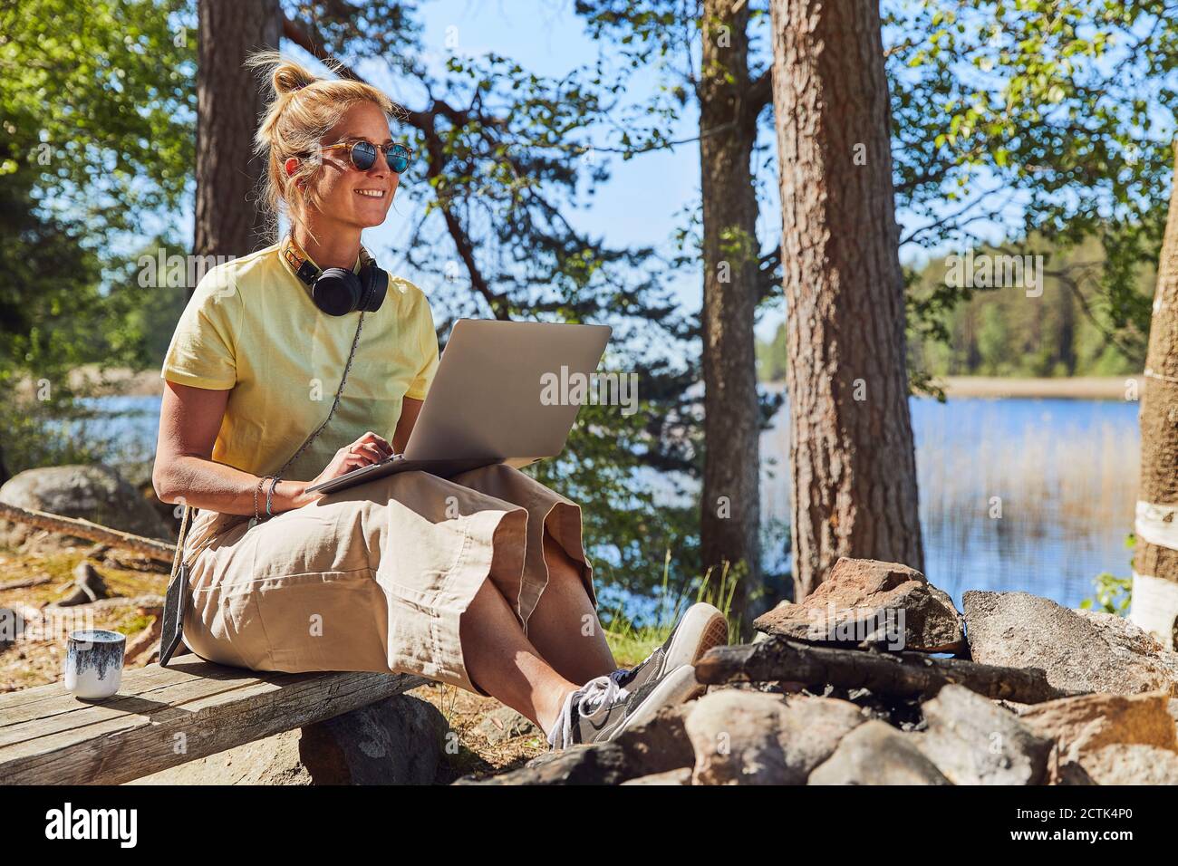 Mid adult woman wearing sunglasses using laptop while sitting in Tiveden National Park, Sweden Stock Photo