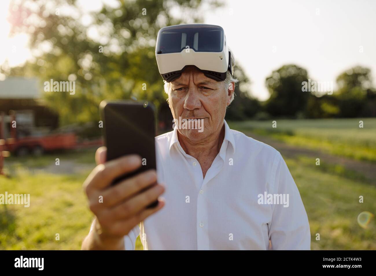 Man using smart phone while wearing VR glasses in yard Stock Photo