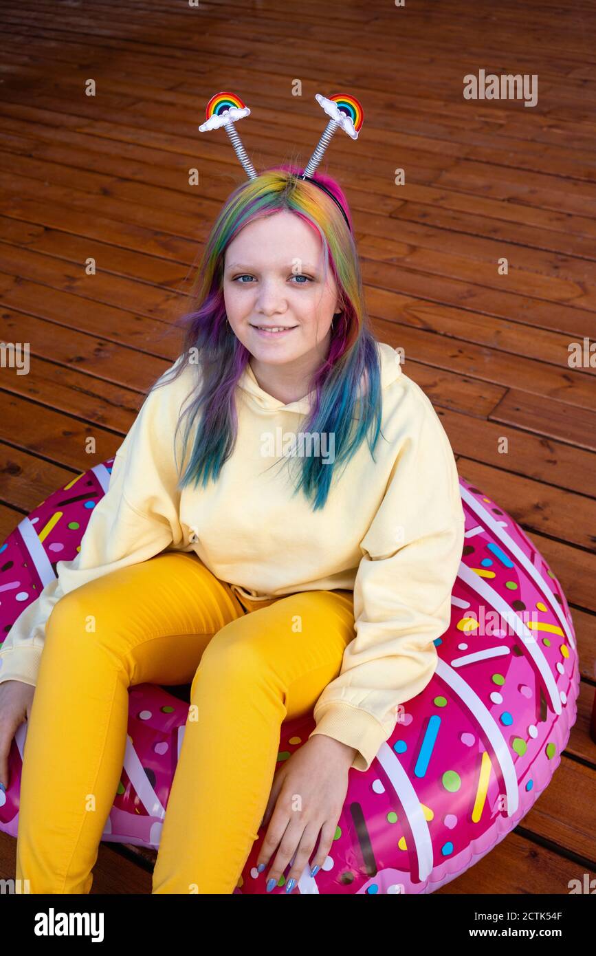 Young woman with dyed hair sitting in floating tyre on wooden ground Stock Photo