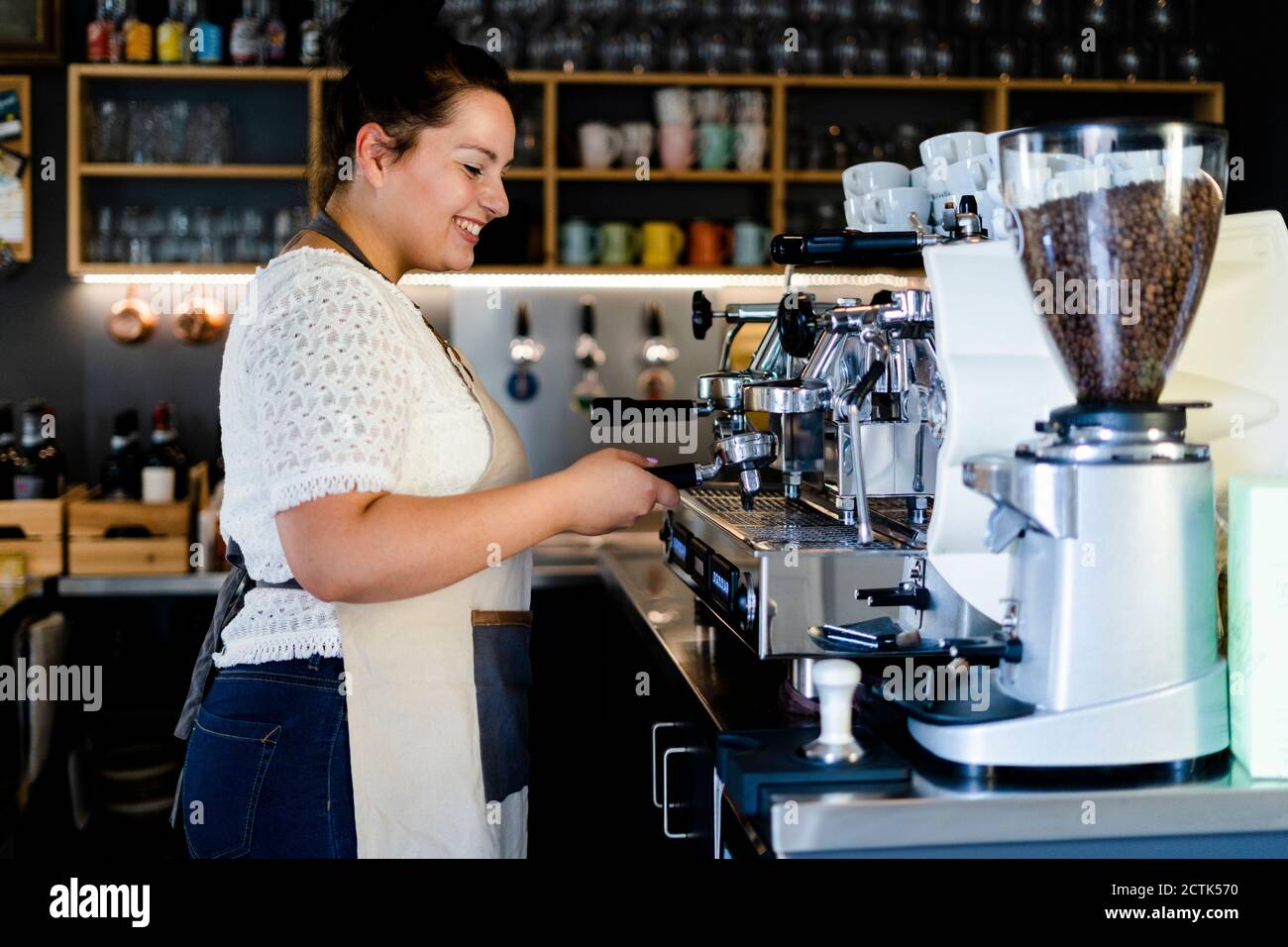 Smiling female barista making coffee through machine in cafe Stock Photo