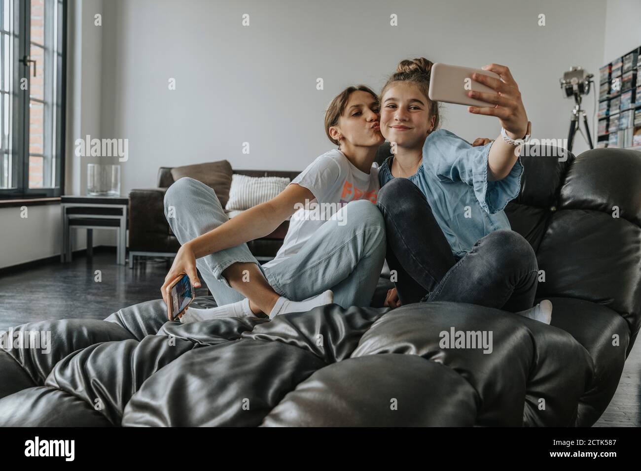 Friends taking selfie with smart phone while sitting on couch at home Stock Photo